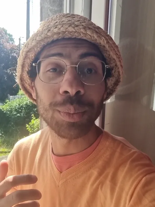 Vie, chemise orange et chapeau de paille, présente son univers face caméra